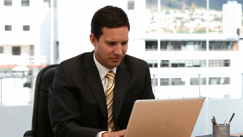 Businessman working on the laptop and looking at the camera in an office