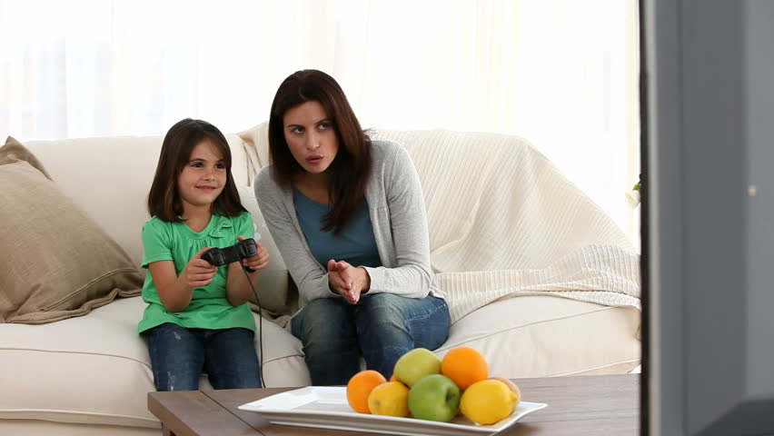 Cheerful mom encouraging her daughter to play video games on the sofa
