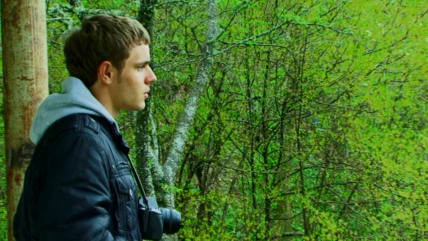 A young man with a camera photographing beautiful green scenery. Two shots.