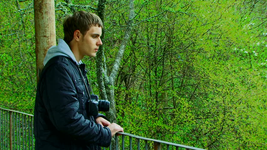 A young man with a camera photographing beautiful green scenery.
