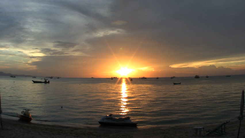 A lovely shot of a sunset on Pattaya Bay, Thailand with a variety of boats and jet skis in the foreground.