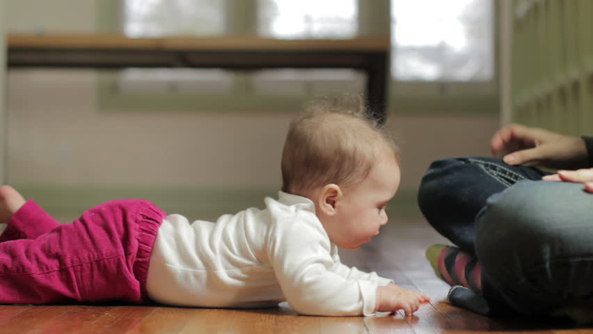 Mother helping baby stand up from the floor, close shot