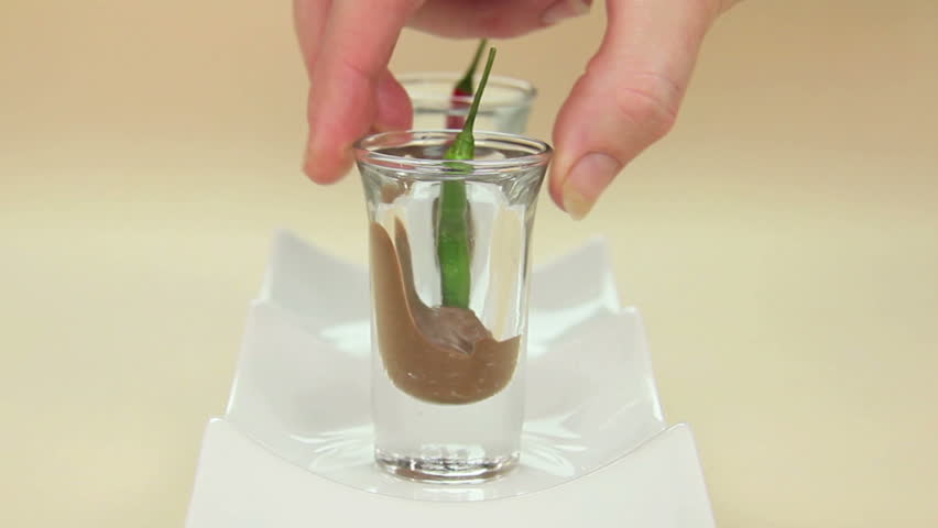 Chillies in chocolate in shot glasses being put down in a line towards camera.