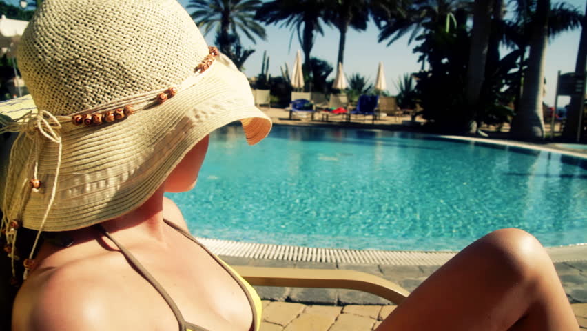 Woman in summer hat sunbathing by the pool