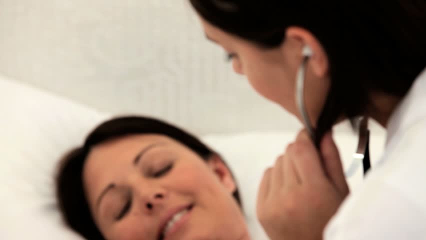 Nurse listening to the belly of her pregnant patient in a bedroom