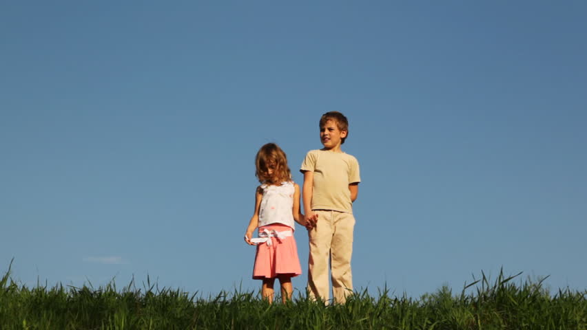 boy and little girl stand on grass, while their mother clicks the clapperboard