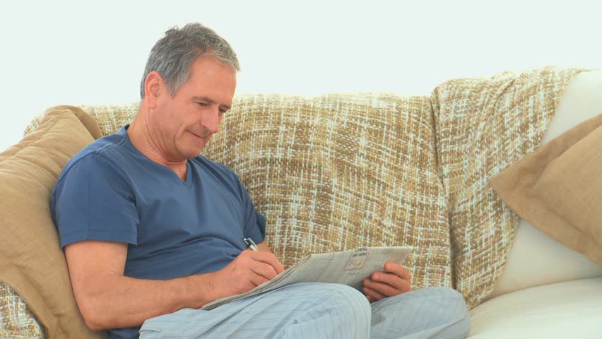 Retired man doing crosswords with his newspaper on his couch