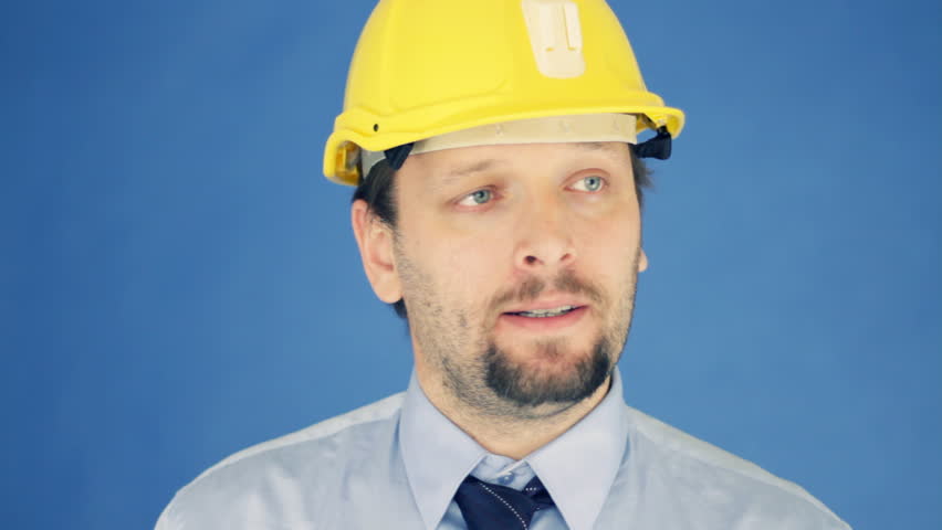 Successful engineer in yellow helmet showing ok sign, on blue background