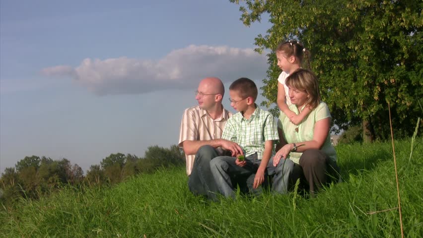 Family with two children sits in a grass and looks afar. Summer day.