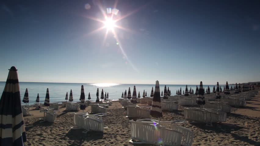 Many parasols and deckchairs standing on beach at sunny day, camera moving in direction of water
