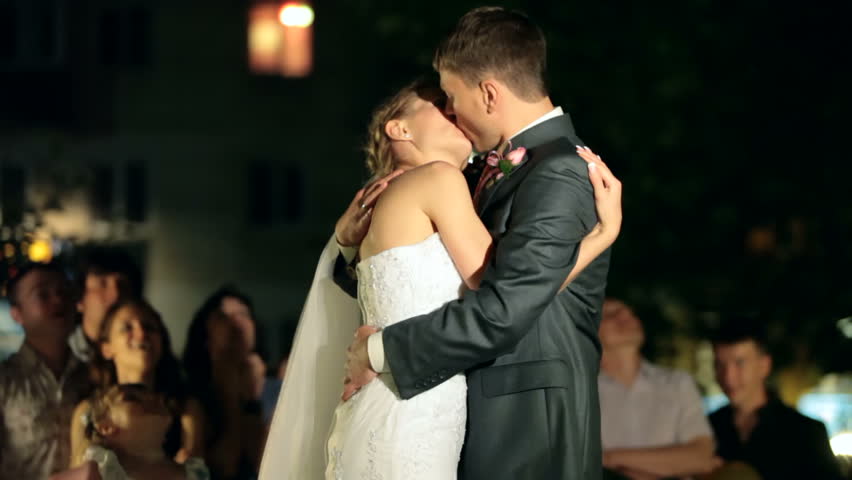 newlyweds kissing at night, surrounded by visitors and relatives