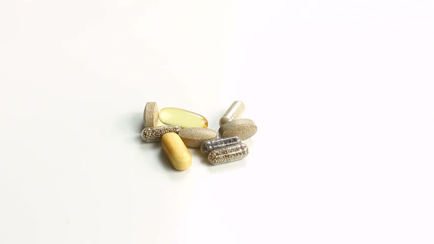 Vitamin A, B, C, D, E pills in tablet, gel, capsule forms pour onto white table. 1080p