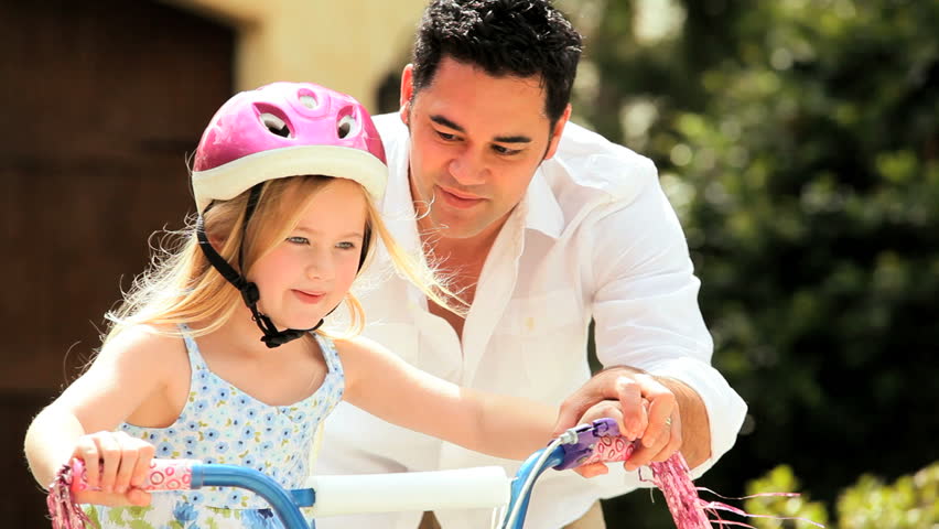Asian father teaching his little blonde daughter to ride a bicycle