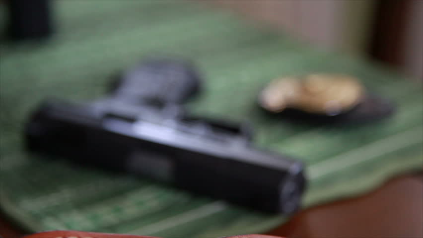 The camera brings in and out of focus a nine millimeter pistol and a detectives or police badge lying on a table