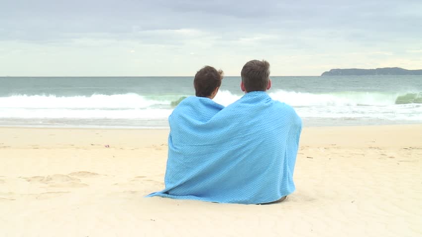 Couple sitting on the beach with a blue towel.