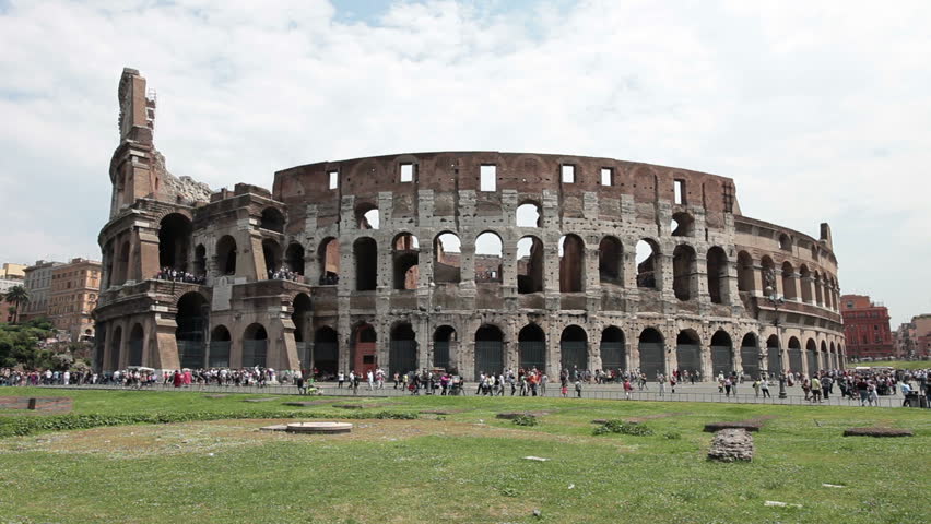 Rome Colosseum tourists across lawn park with tourists visiting the ancient and famous landmark. Home of the Gladiator events. One of the most recognizable buildings in the world.