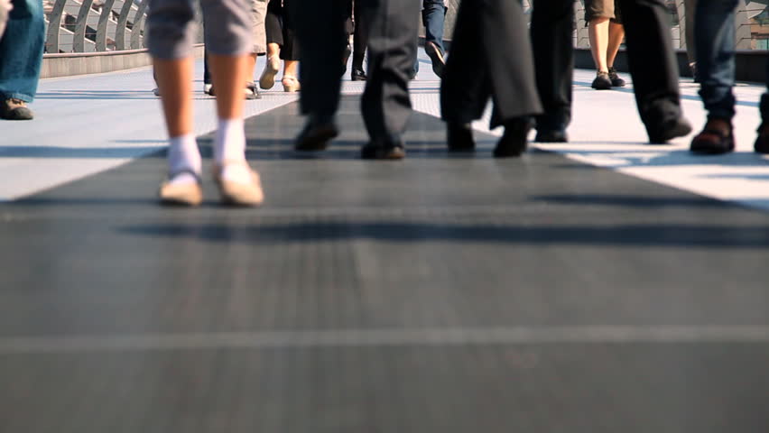 A group of young people walk across the Golden Jubilee Bridge over the River Thames in London. Shot from a low angle, only their legs are visible and there is a very narrow depth of focus.