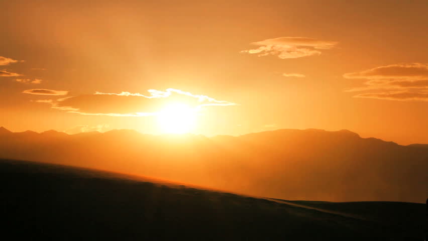 Lone female hiker in silhouette walking over sand dunes into the sun in a desert environment