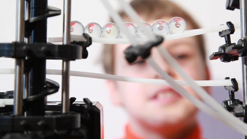 Boy looks at marbles inside run machine which reflect his head, closeup view