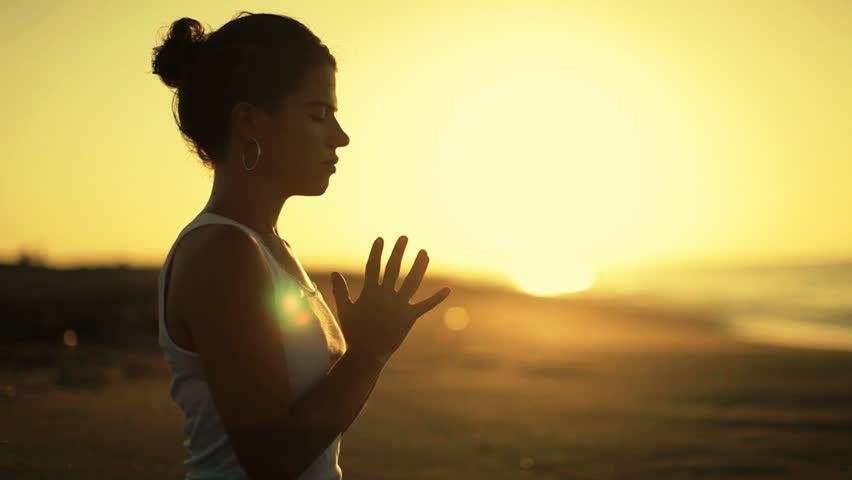 young woman practices yoga on a beach at sunrise