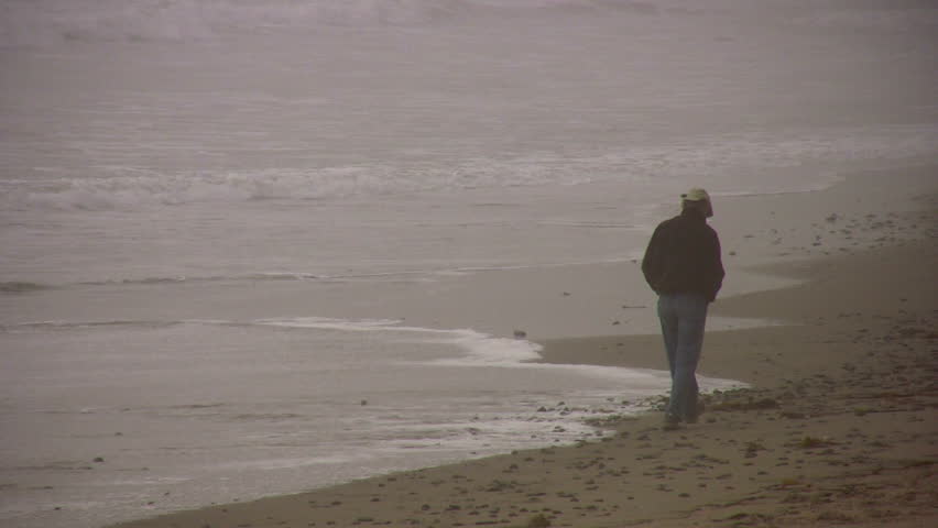 Man in a cowboy hat walks on a beach in the fog.