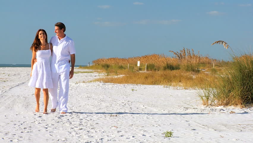 Attractive healthy couple enjoying time together walking barefoot on the beach filmed at 60FPS