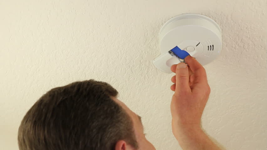 Adult man changing the 9-volt battery in his home ceiling fire alarm to protect his family from danger.