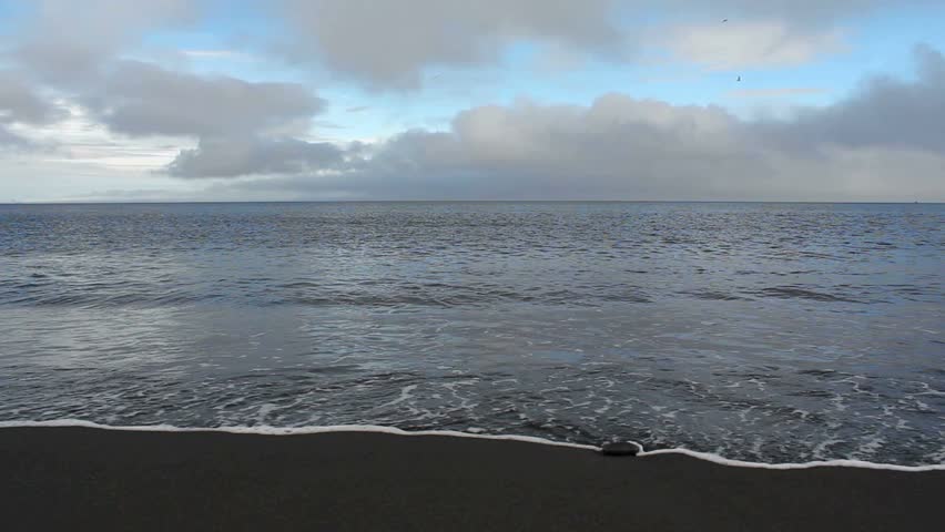 Waves roll towards shore, engulf sand, retreat, create a beautiful reflection of clouds and blue sky. 1080p 