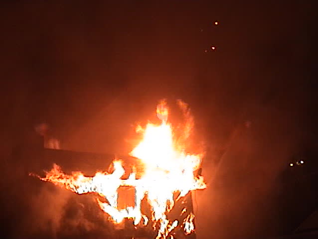 Flames engulf a house as a ladder truck sprays water.