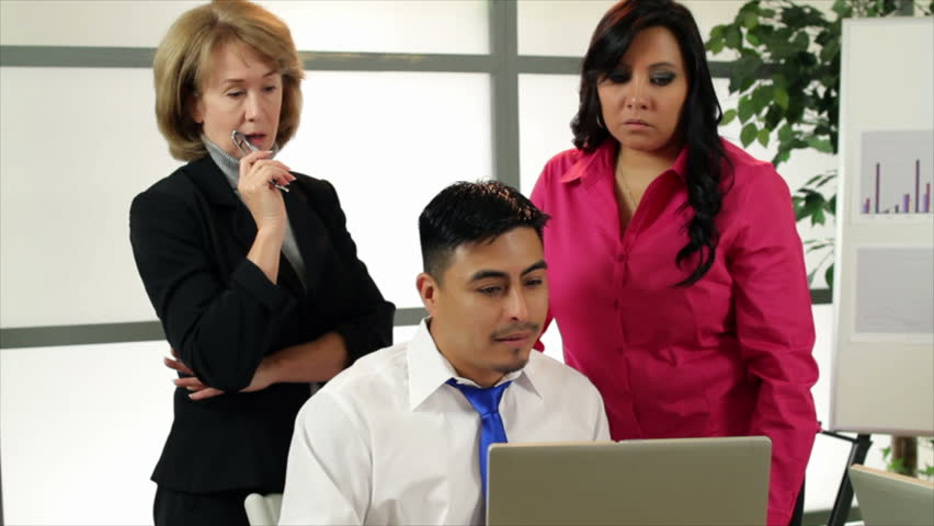 A mature business woman and her two young Hispanic co-workers discuss what is on the laptop. Camera tracks to the left.