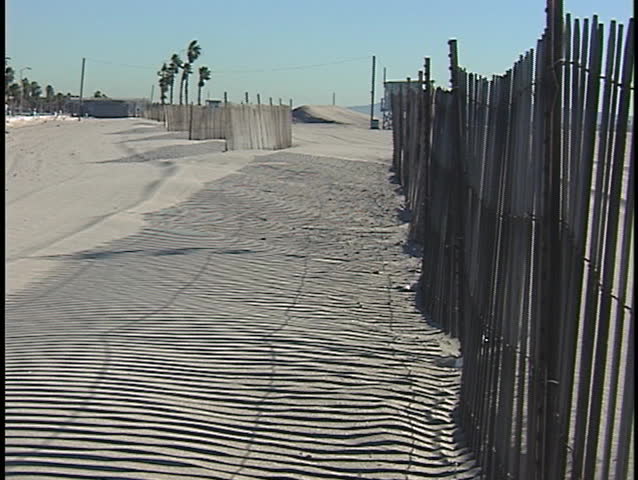 A fence casts shadows onto a bare sandy beach.