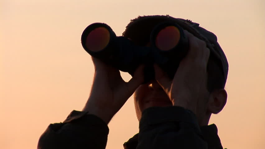 young man looking through binoculars at sunset
