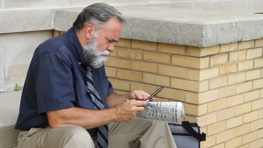Man uses his cellphone to call about a job listing in the newspaper.