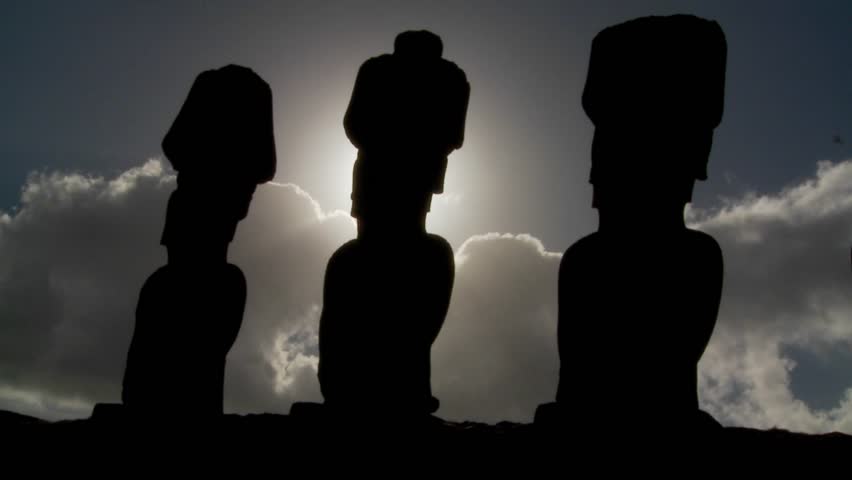Easter Island statues are silhouetted against the sun.