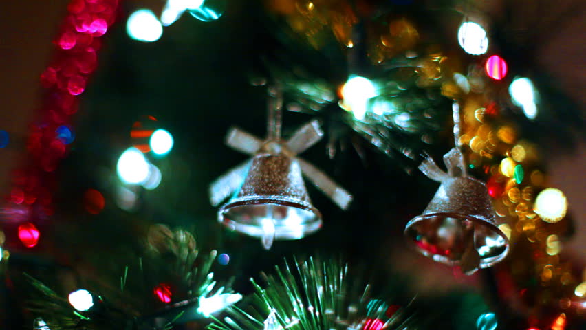 two gold toy bells hang on Christmas tree among of blinking colored garlands, close-up