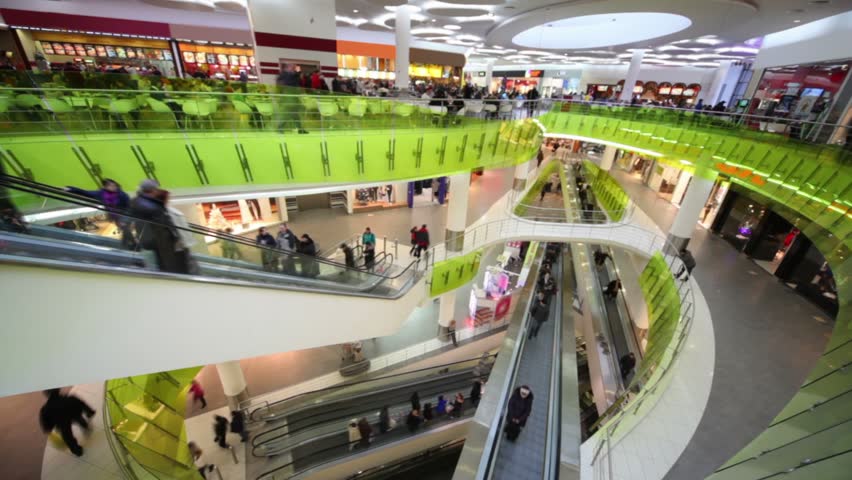 Many peoples move on escalators in multiple floors shopping center, border illumination change light color, view from above