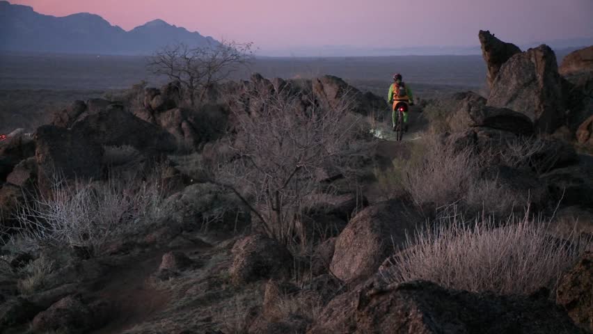 Cyclists travel rough trails in a desert area near dusk with head lights