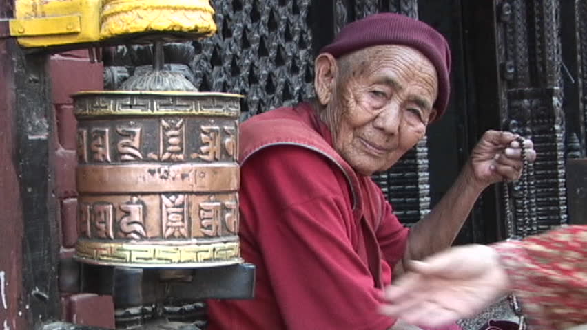 KATHMANDU, NEPAL - CIRCA 2005: Old Buddhist monk (or nun) with prayer beads next to spins prayer wheel circa 2005 in Kathmandu.