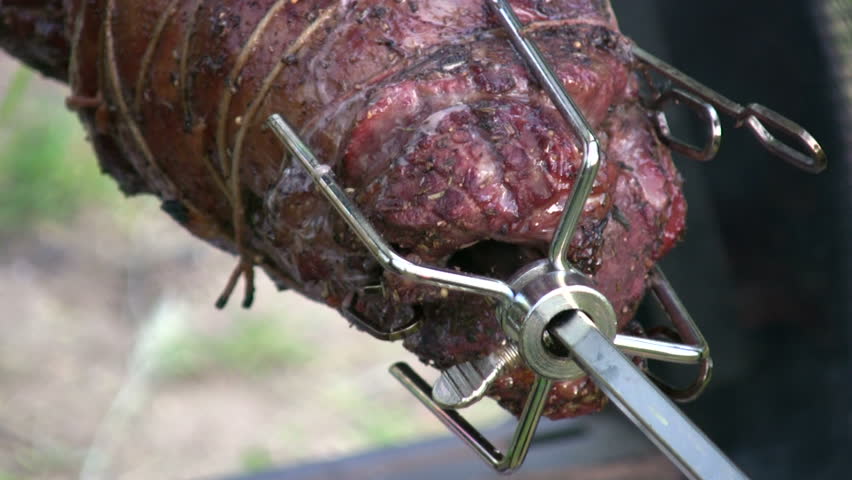 detail of savory meat roasting on a spinning rotisserie with smoke, dripping juices, and flame reflections