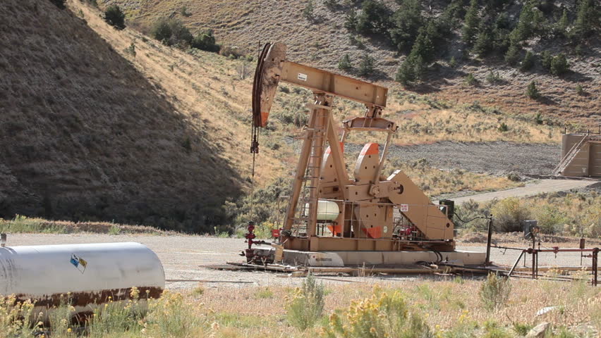 Oil well pumping crude from deep valley between mountains in central Utah. Propane motor powers the pump that extracts the oil. Fast motion.