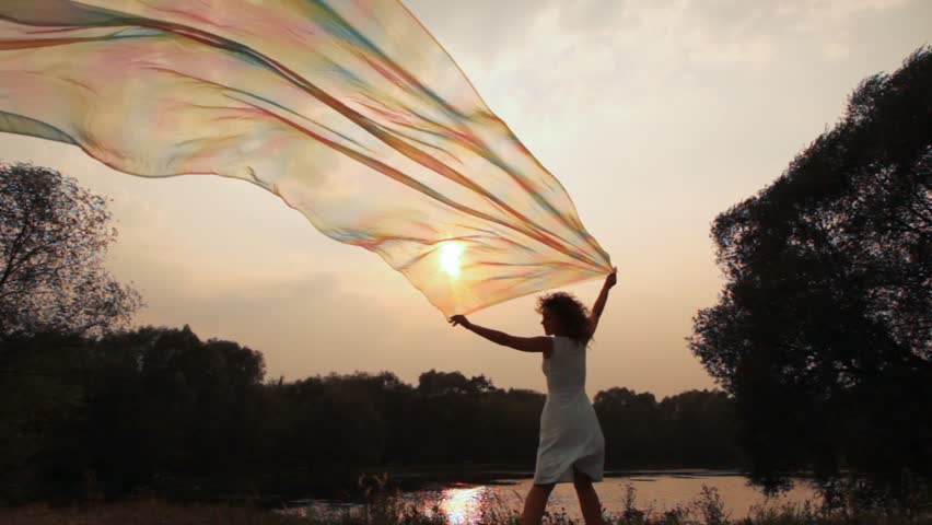 woman stands on bank of lake and holds shawl which fluttering gets to camera