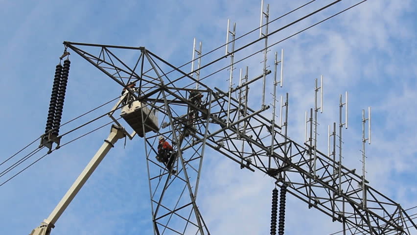 A hydro worker descends from an electric power station tower in a lift bucket.