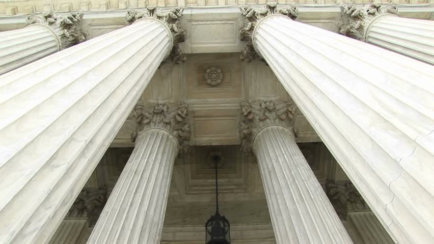 View of columns, a hanging lamp, and bronze doors at the west entrance of the Supreme Court.