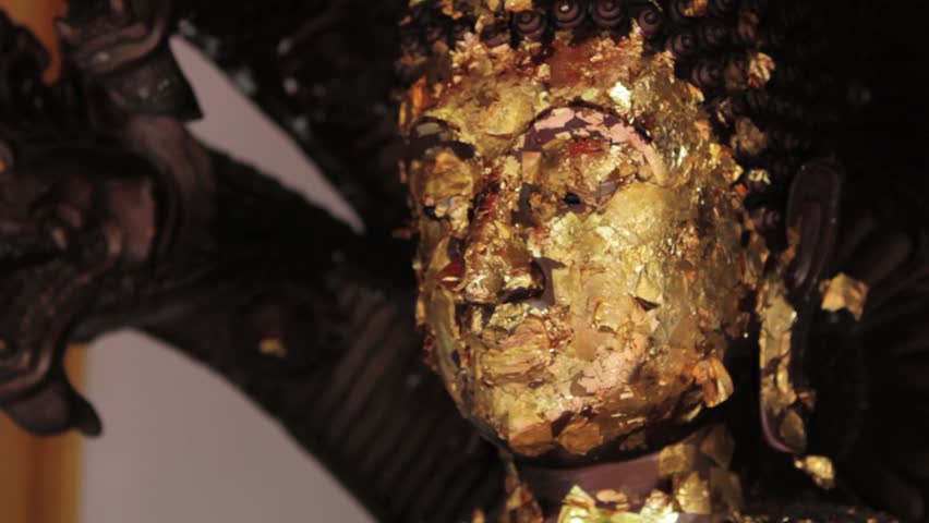 A buddha statue with gold flakes waving in the breeze that have been placed on it to earn merit.