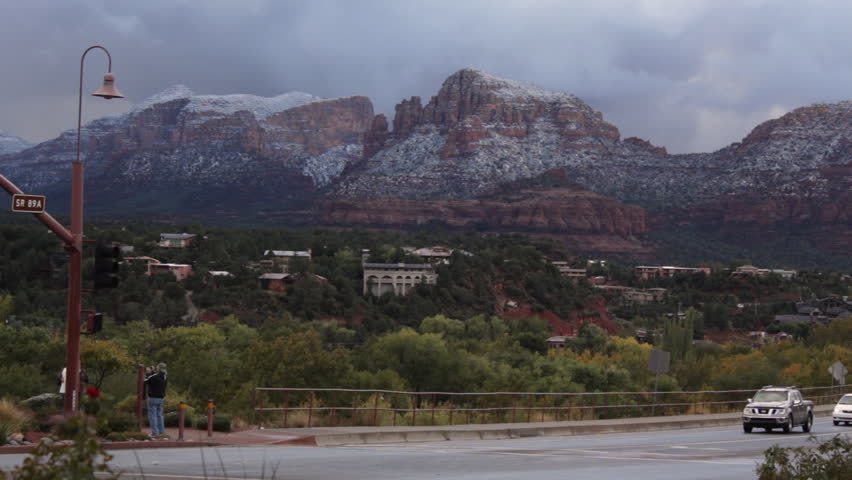 Clouds move slowly over the mountains of Sedona, Arizona after a light dusting of snow in the morning. Shot in Uptown Sedona with traffic in foreground.