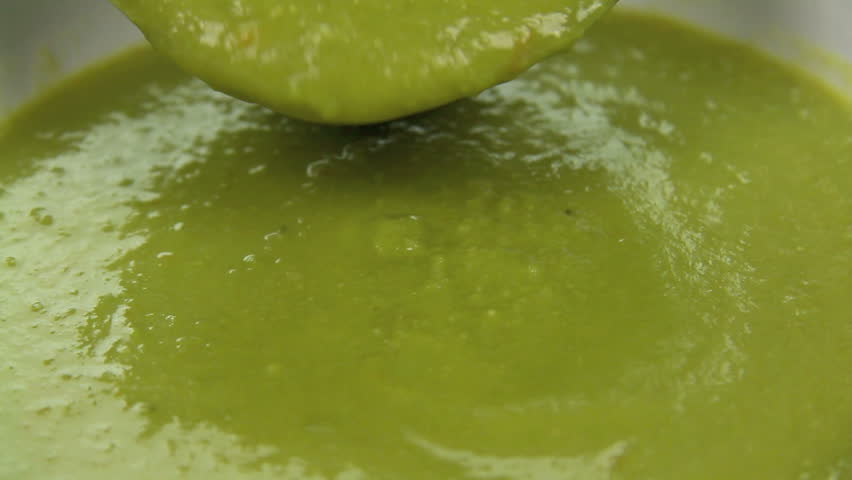 Close up of pea soup being poured into a bowl with a ladle.