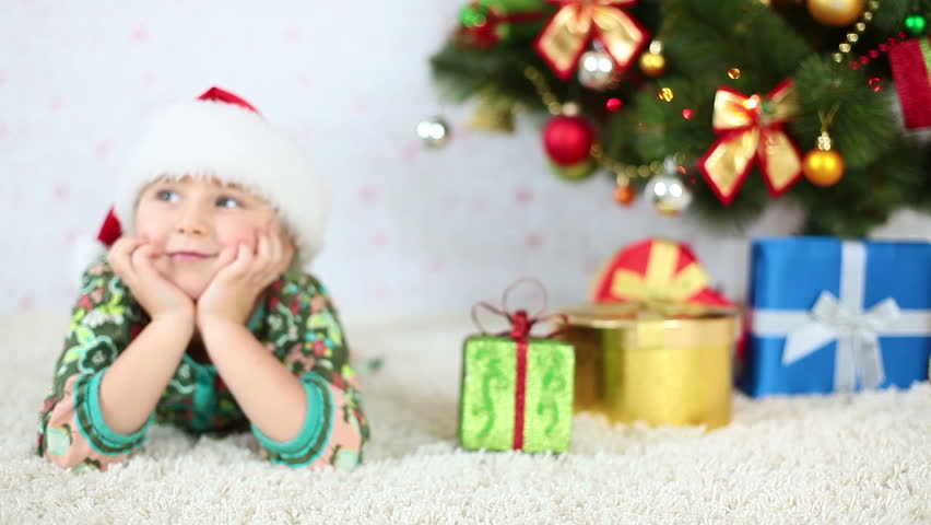 Smiling girl in Santa hat lying near the Christmas Tree