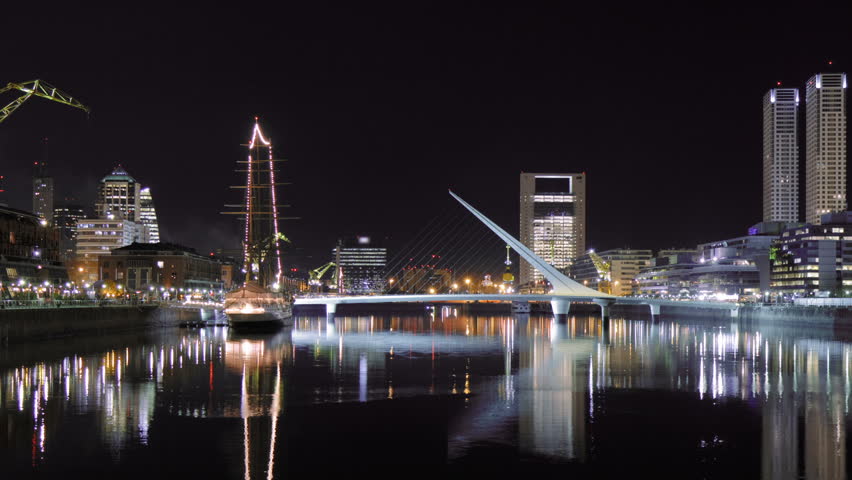 Puerto Madero harbor, an exclusive district of Buenos Aires, Argentina, at night. People rush along the boardwalks and a landmark footbridge. Photo time-lapse with cg-zoom out (Aug 2010, DSLR).