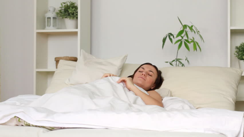 Young attractive woman waking up and stretching in bed, dolly shot