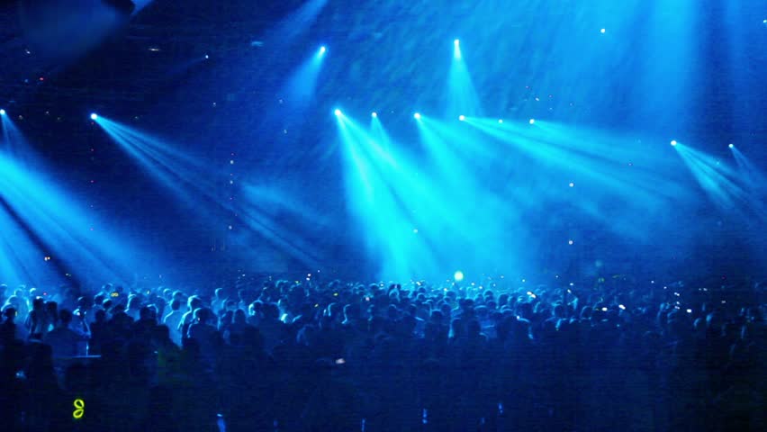 Crowd at rave party, people dance in blue light of projectors